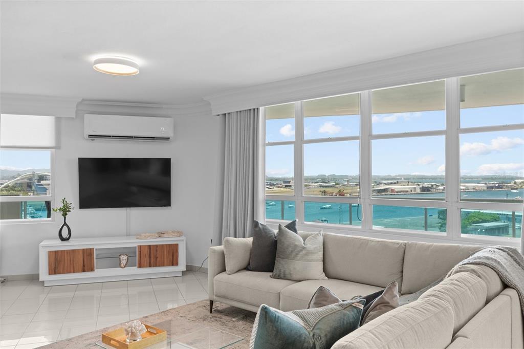 A living room with a white sofa, media console, and large windows overlooking the water — 550 AVE DE LA CONSTITUCION UNIT 1010, SAN JUAN, PR