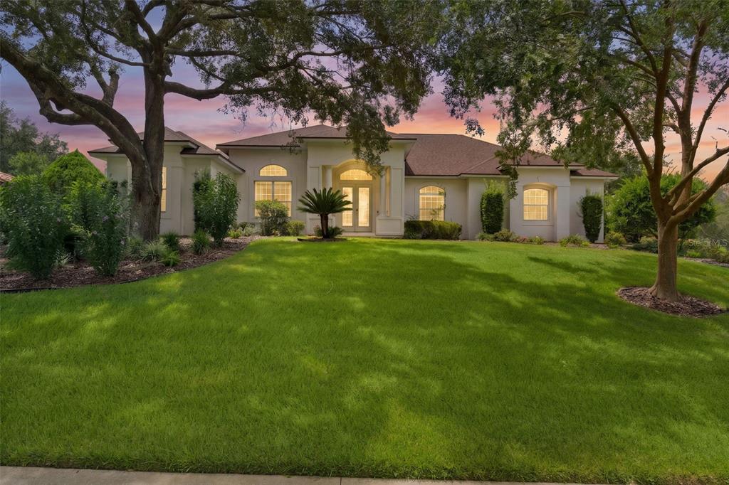 A single-story house with a light-colored exterior, arched entryway, and large trees on the lawn — 39407 TREELINE DRIVE, LADY LAKE, FL