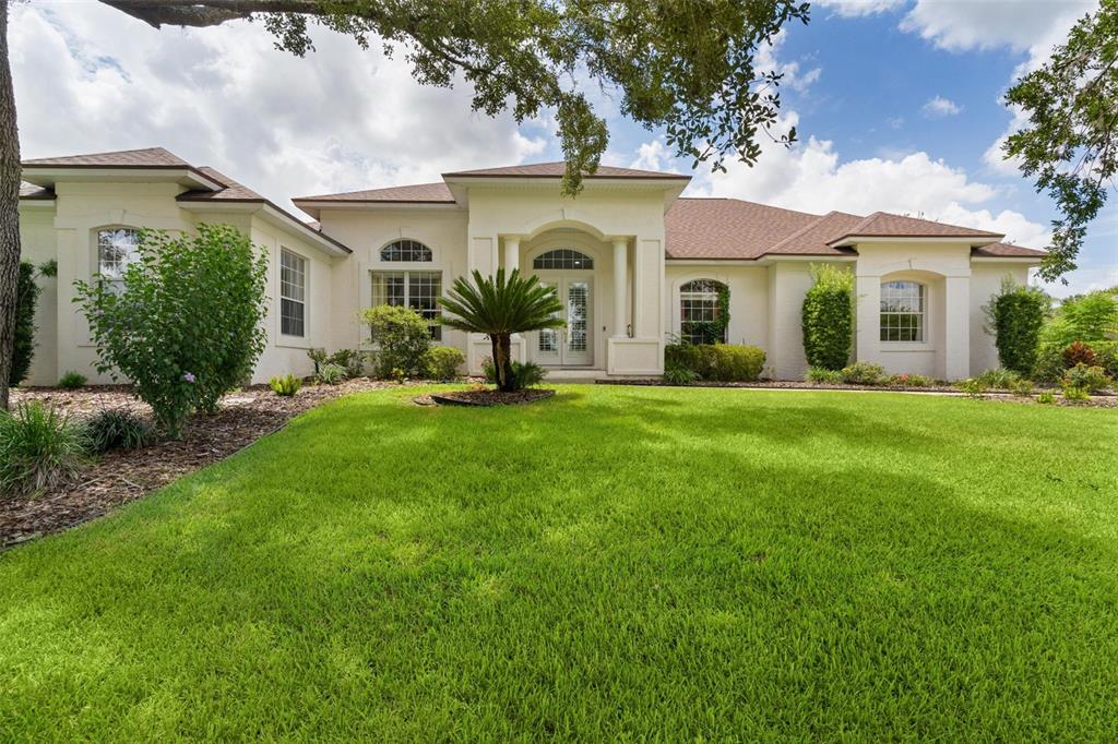 A single-story house with a cream-colored exterior, a brown shingled roof, and a green lawn — 39407 TREELINE DRIVE, LADY LAKE, FL