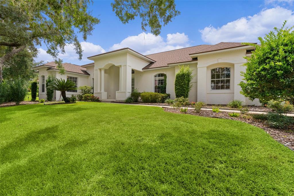 A single-story house with a white stucco exterior, a brown roof, and a green lawn — 39407 TREELINE DRIVE, LADY LAKE, FL