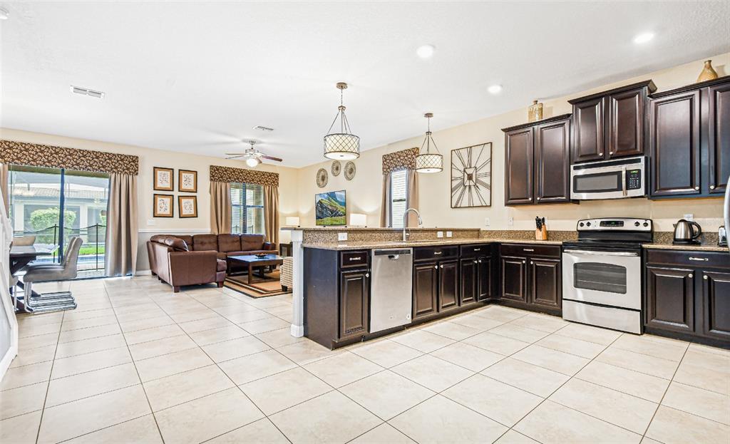 A kitchen features dark wood cabinets, stainless steel appliances, granite countertops, and light tile flooring — 9026 SHADOW MOUNTAIN STREET, DAVENPORT, FL