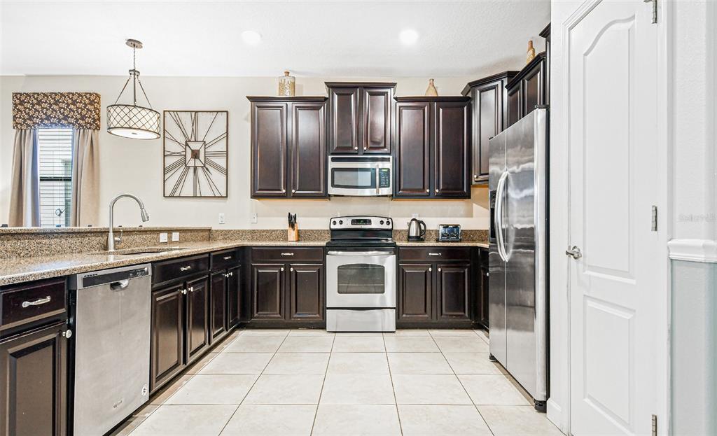 A kitchen with dark wood cabinets, granite countertops, and a breakfast bar with four stools — 9026 SHADOW MOUNTAIN STREET, DAVENPORT, FL