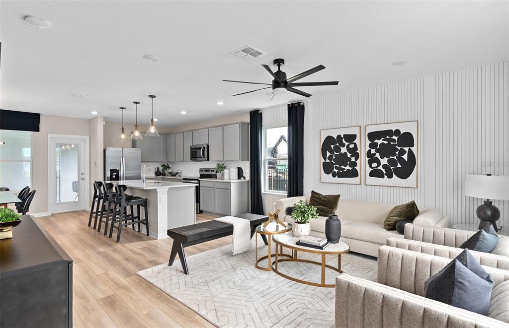 An open-concept living room and kitchen feature light wood floors, gray cabinetry, and modern decor — 10927 HEATHER HAVEN STREET, ORLANDO, FL