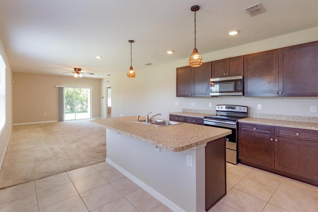 A kitchen with dark wood cabinets and a granite island overlooks a carpeted living area — 3075 GIBRALTAR BOULEVARD, NEW SMYRNA BEACH, FL