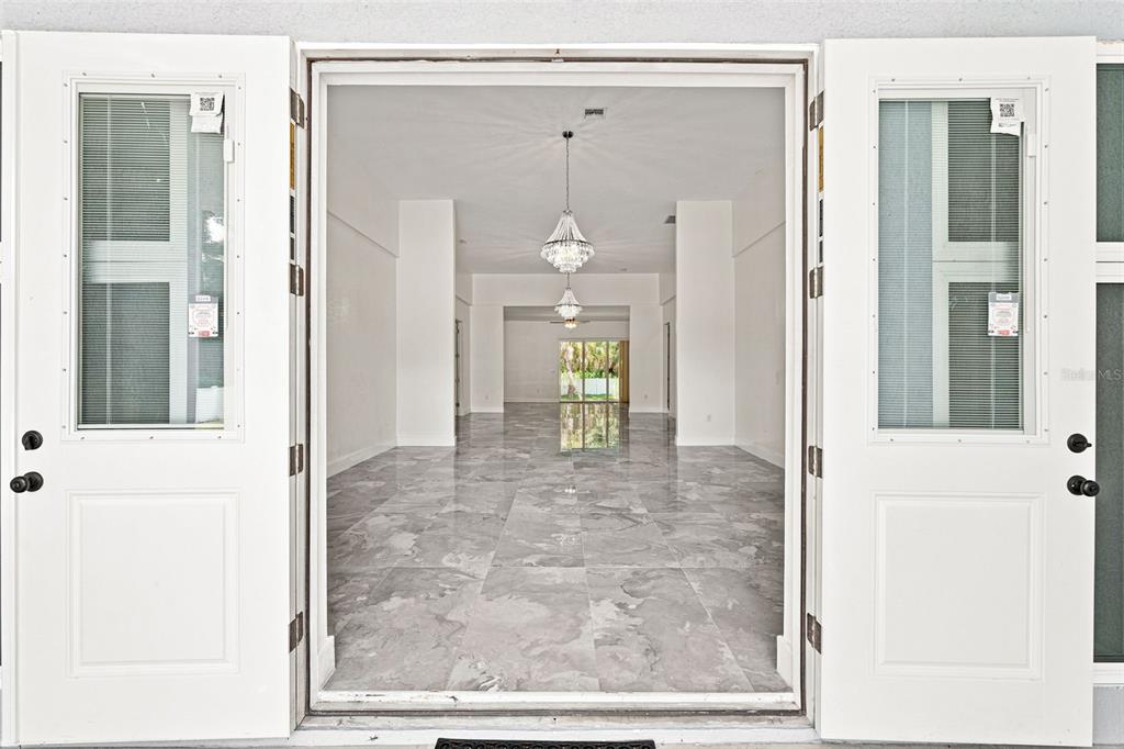 A view through open double doors into a bright, empty room with marble-look tile flooring — 1853 DELLA DRIVE, NAPLES, FL