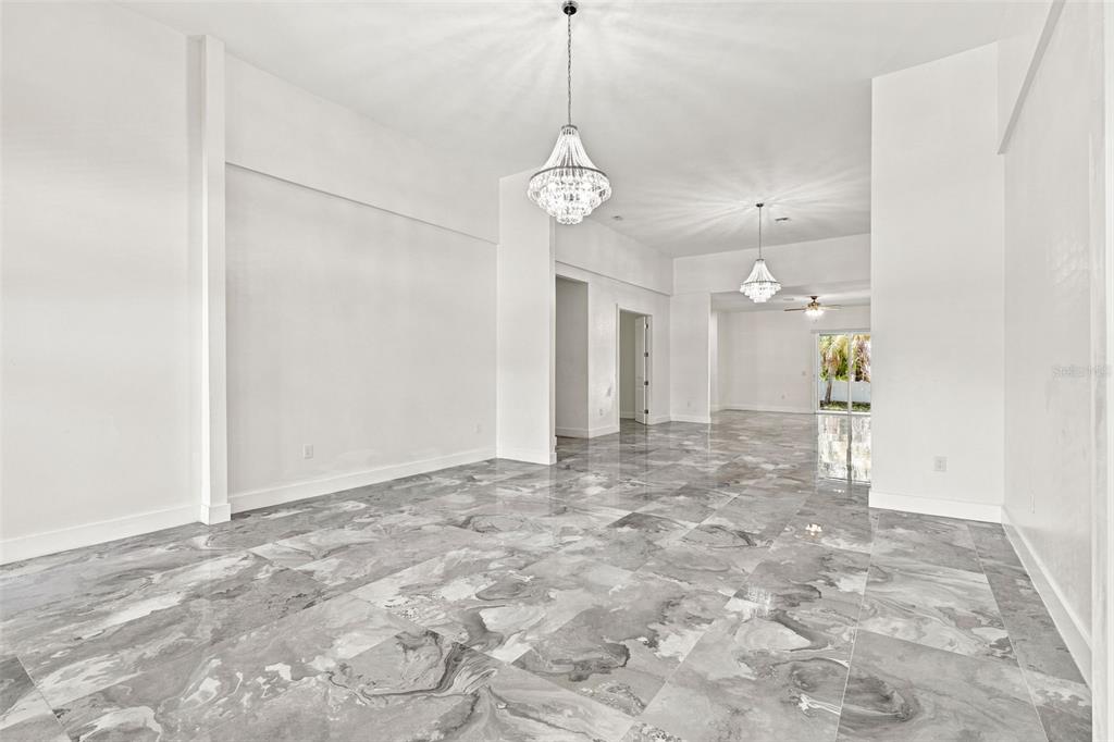 A spacious room with high ceilings, two crystal chandeliers, and gray marble-patterned tile flooring — 1853 DELLA DRIVE, NAPLES, FL