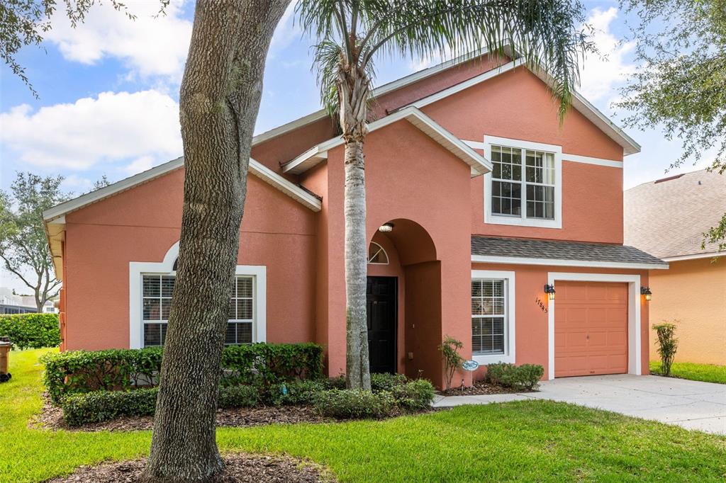A two-story house with peach-colored stucco, a single-car garage, and a palm tree in front — 17845 WOODCREST WAY, CLERMONT, FL