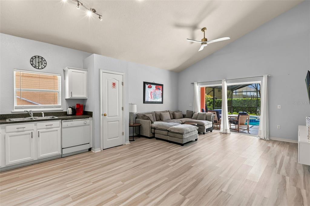 A living room with light wood flooring, a gray sectional sofa, and an open kitchen area — 17845 WOODCREST WAY, CLERMONT, FL