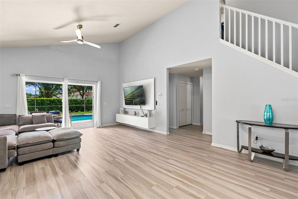 A living room features light wood flooring, a vaulted ceiling, and a sliding door to a pool — 17845 WOODCREST WAY, CLERMONT, FL