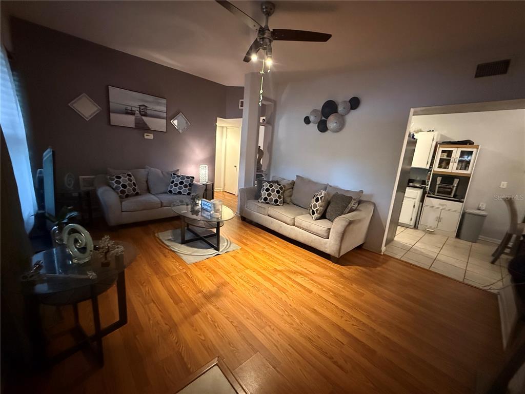 A living room with hardwood floors, two grey sofas, and an adjacent kitchen area — 1435 TRIANGLE DRIVE, MOUNT DORA, FL