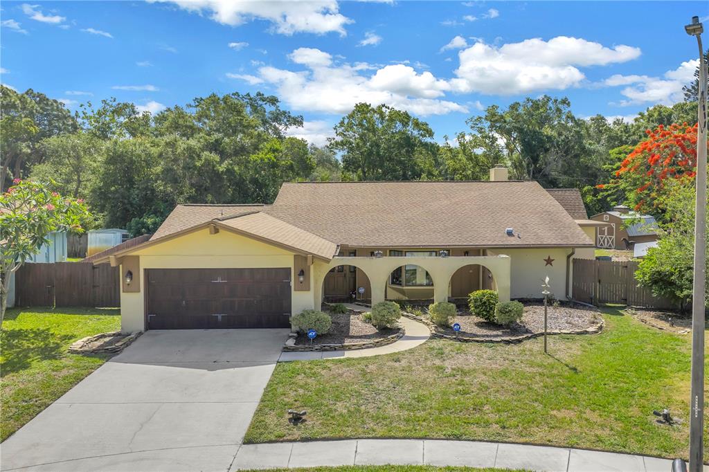 A single-story house with a brown roof, arched entryway, and attached garage sits on grass — 10657 DEL PRADO DRIVE E, LARGO, FL