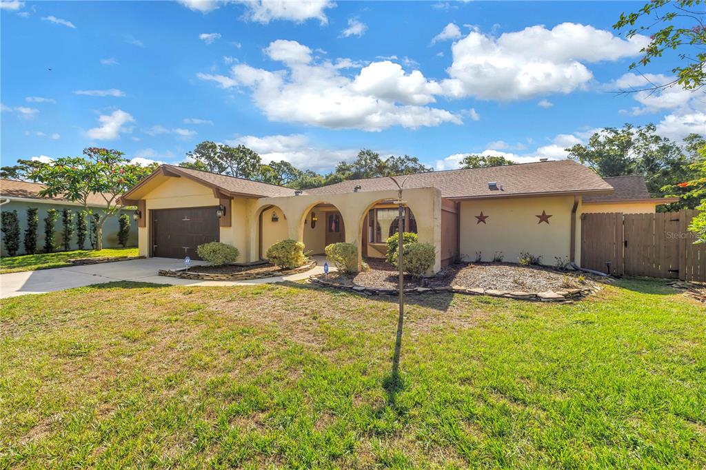 A single-story house with a tan stucco exterior, arched entryway, and a two-car garage — 10657 DEL PRADO DRIVE E, LARGO, FL
