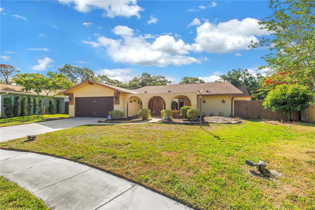 A single-story house with a tan stucco exterior, arched entryway, and a two-car garage — 10657 DEL PRADO DRIVE E, LARGO, FL