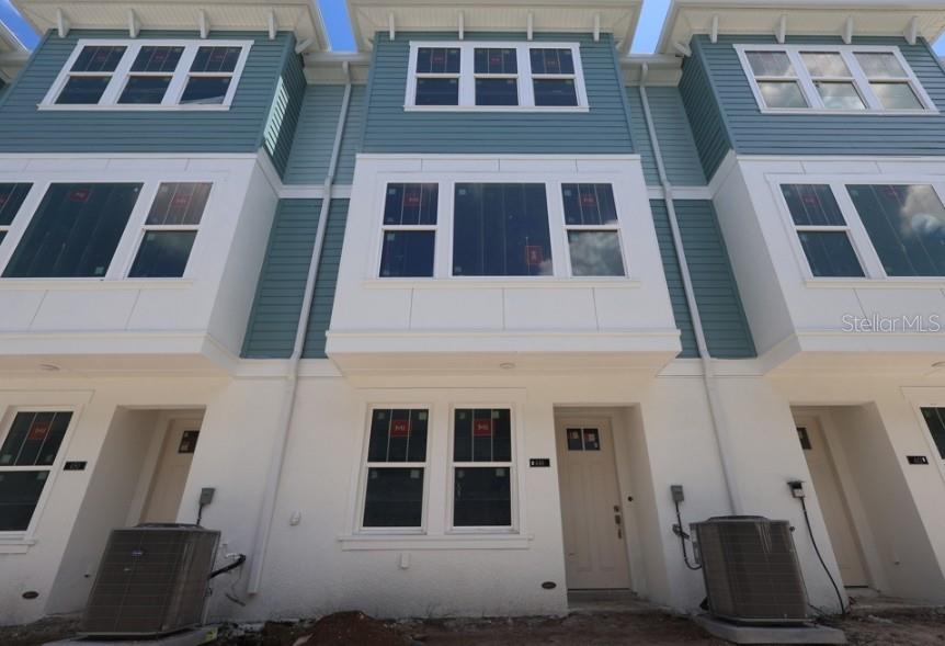 A low-angle exterior view of three attached townhomes with blue siding and white stucco bases — 446 31ST WAY N, ST PETERSBURG, FL