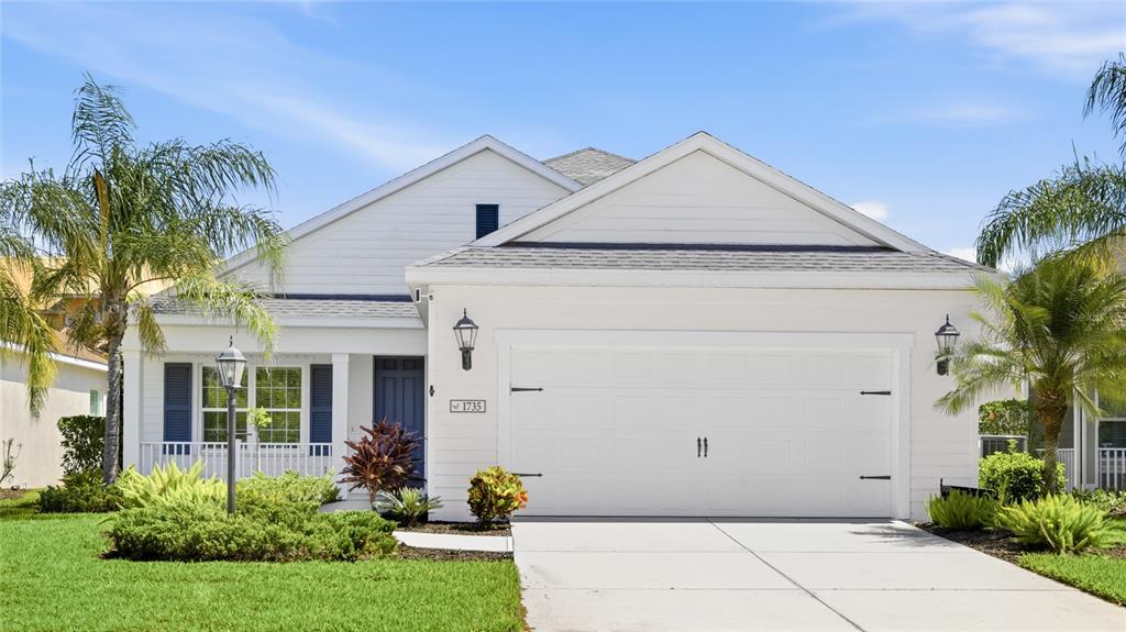 A white single-story house with a two-car garage and blue shutters under a blue sky — 1735 LAKE VERONA CIRCLE, BRADENTON, FL