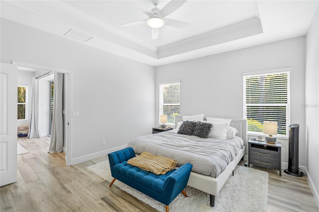 A bedroom features a tray ceiling, light wood-look flooring, a bed with a blue bench, and two windows — 1735 LAKE VERONA CIRCLE, BRADENTON, FL