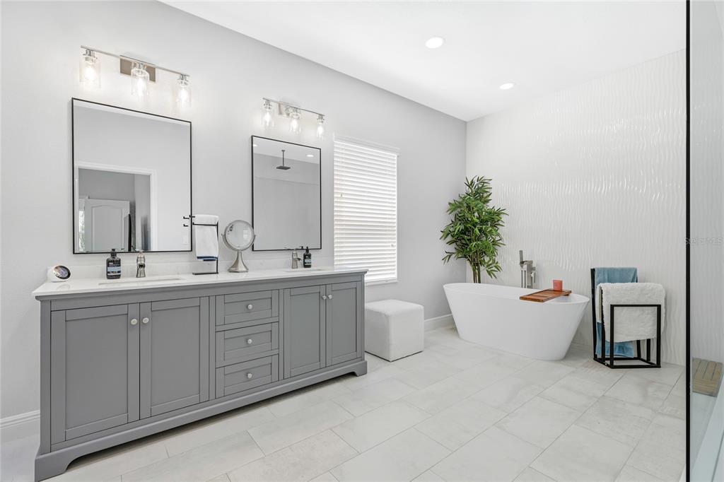 A modern bathroom features a gray double vanity, a freestanding tub, and white tile flooring — 1735 LAKE VERONA CIRCLE, BRADENTON, FL