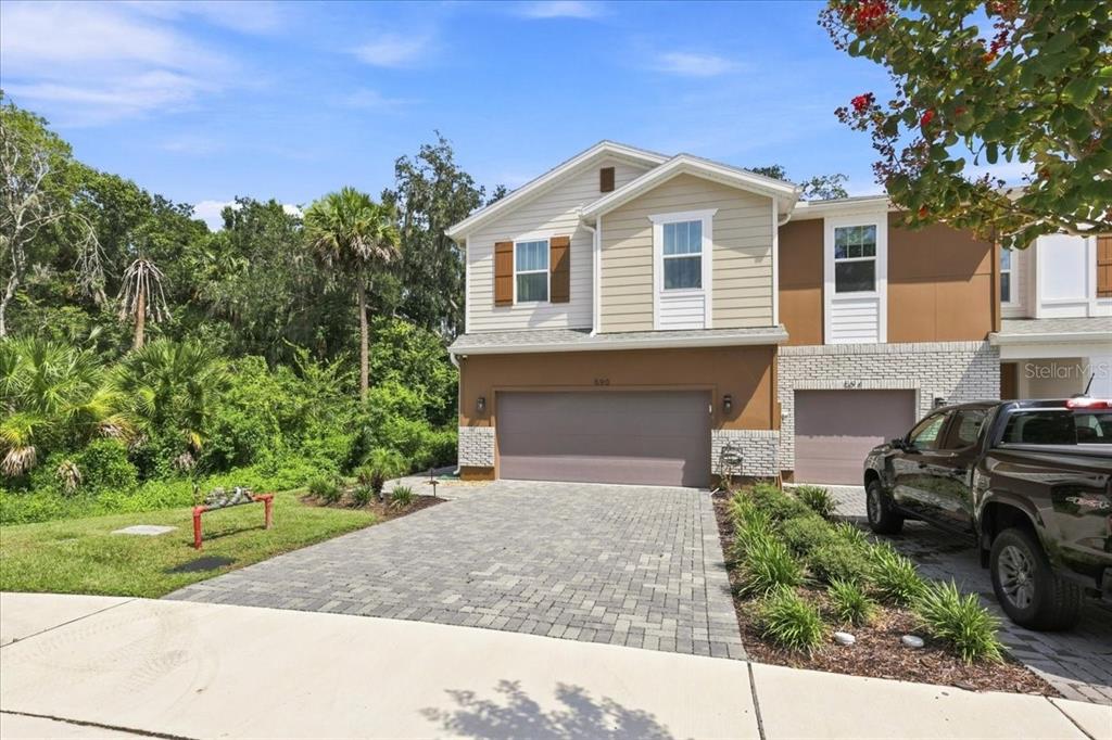 A two-story townhouse with a paved driveway, a two-car garage, and surrounding lush greenery — 590 SOUTHERN EDGE WAY, SANFORD, FL