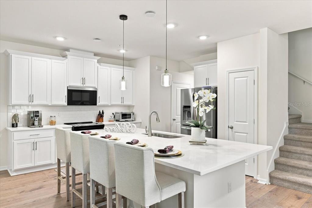 A modern kitchen features white cabinetry, a large quartz island with seating, and stainless appliances — 590 SOUTHERN EDGE WAY, SANFORD, FL