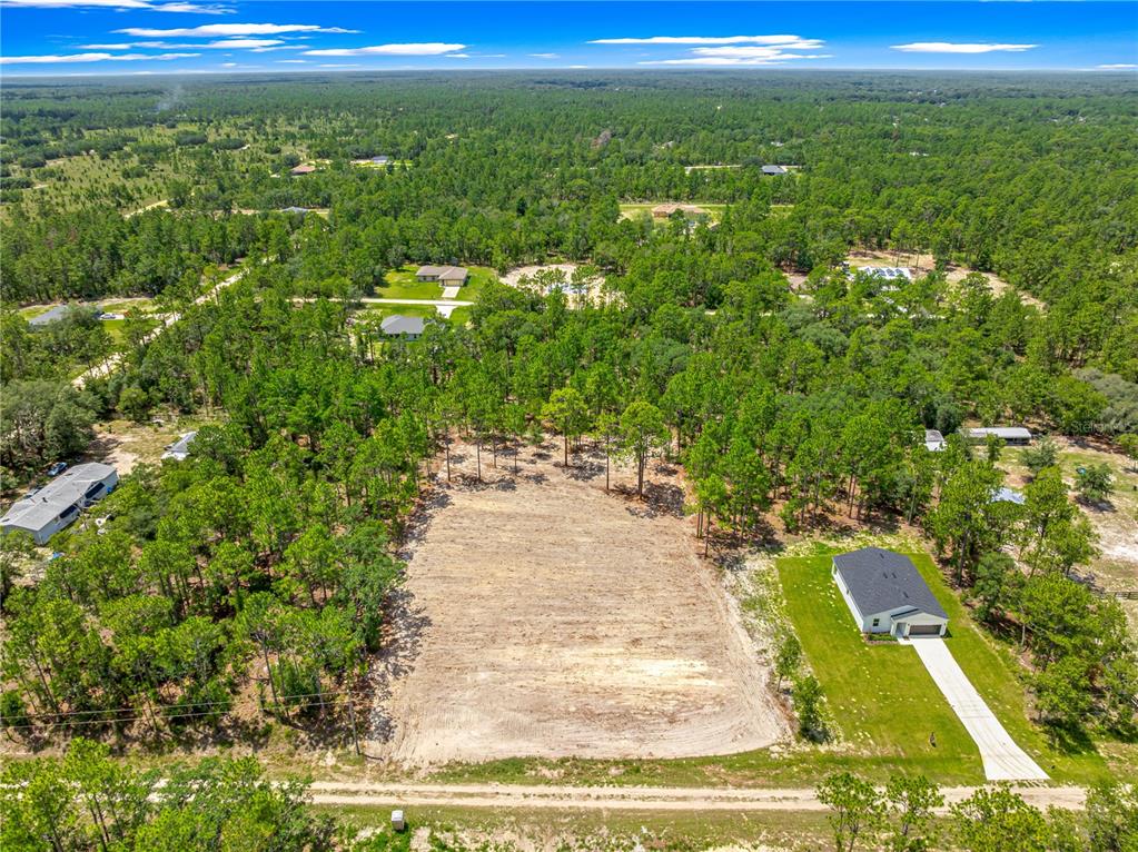 An aerial view shows a cleared rectangular lot situated between two houses and dense forest — 12202 SW 90 PLACE, DUNNELLON, FL