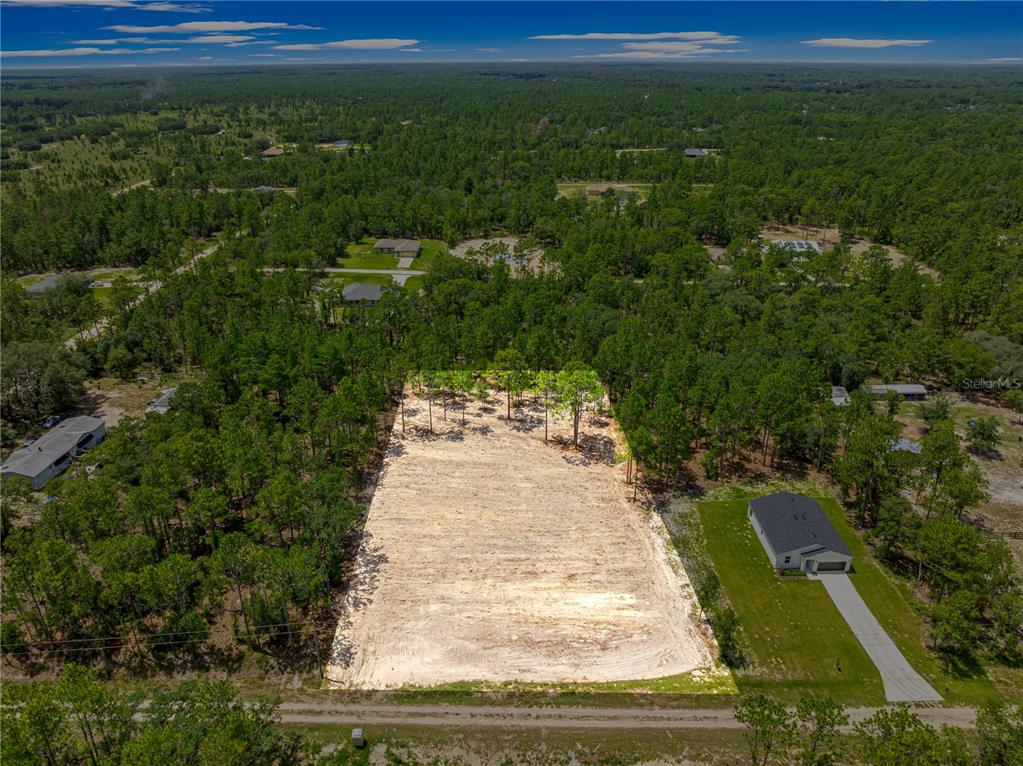 An aerial view shows a cleared, rectangular residential lot surrounded by trees and nearby houses — 12202 SW 90 PLACE, DUNNELLON, FL