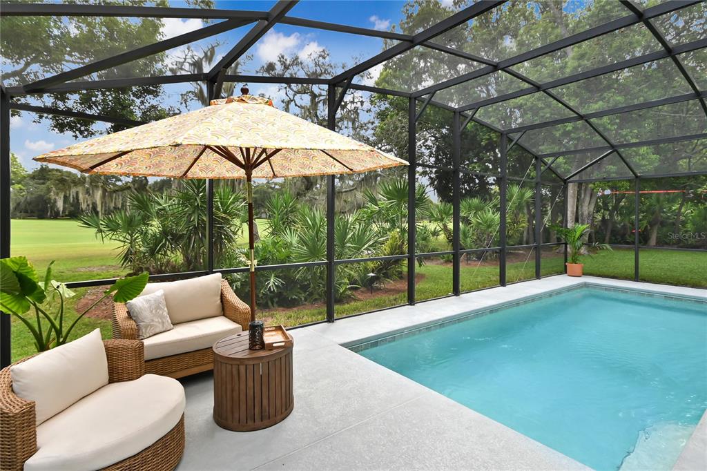 A screened-in patio features a swimming pool, wicker furniture, and a patterned umbrella — 550 BOTTLEBRUSH COURT, NEW SMYRNA BEACH, FL