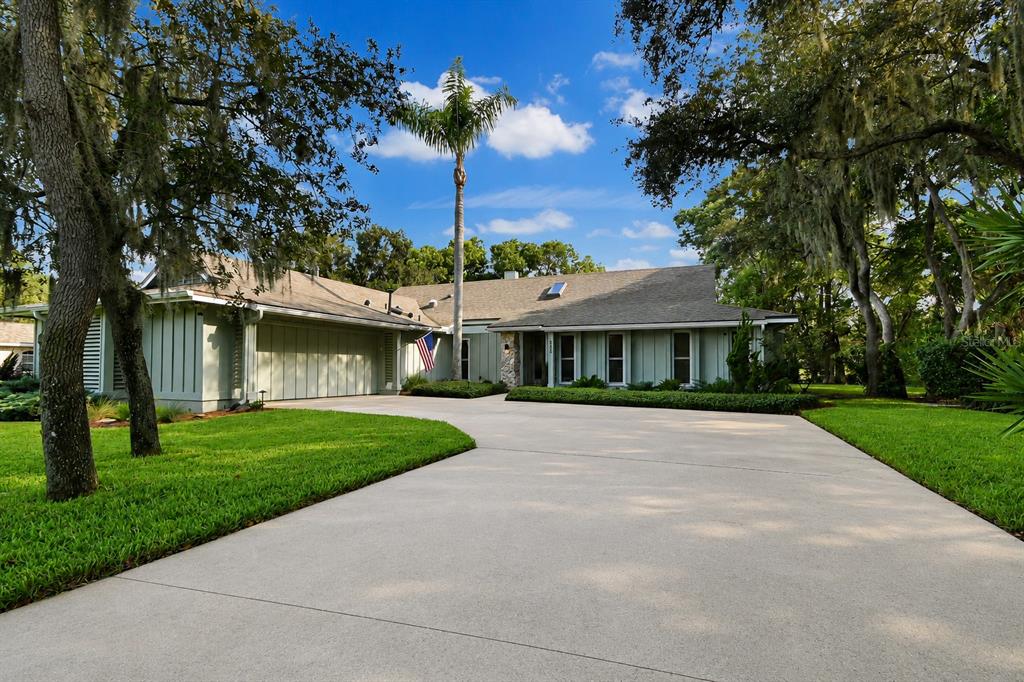 A single-story house with light green vertical siding, a large driveway, and mature oak trees — 550 BOTTLEBRUSH COURT, NEW SMYRNA BEACH, FL