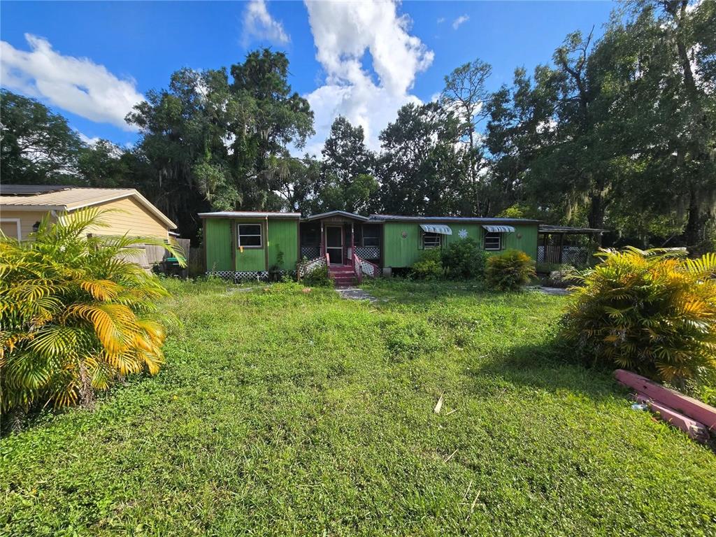 A green manufactured home sits on a grassy lot surrounded by trees and palm plants — 17208 MERCURY ROAD, ORLANDO, FL