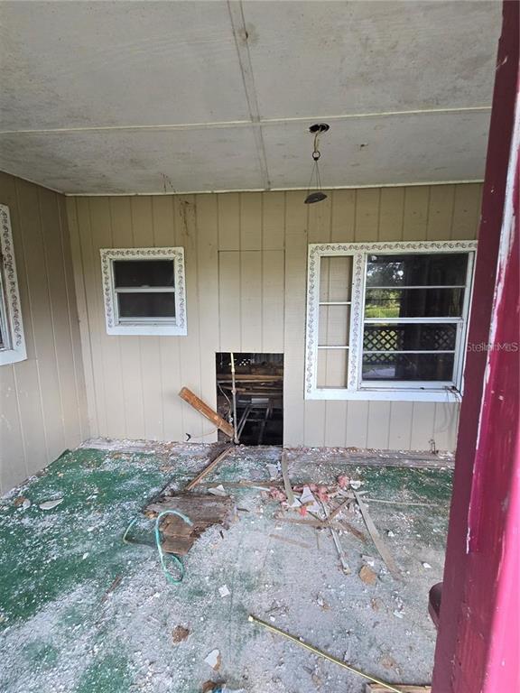 An unfinished porch with exposed wall framing, debris on the floor, and a ceiling light — 17208 MERCURY ROAD, ORLANDO, FL