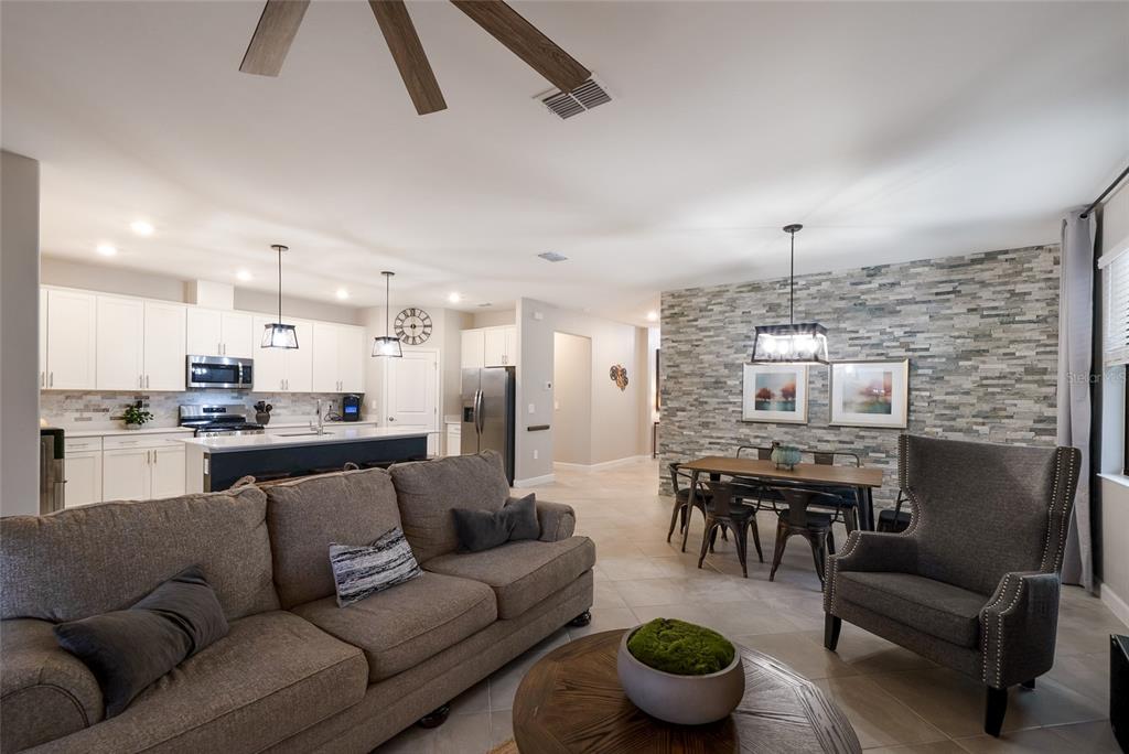 A living room features a stone accent wall, gray furniture, and a large ceiling fan — 15041 SERENE SHORES LOOP, BRADENTON, FL