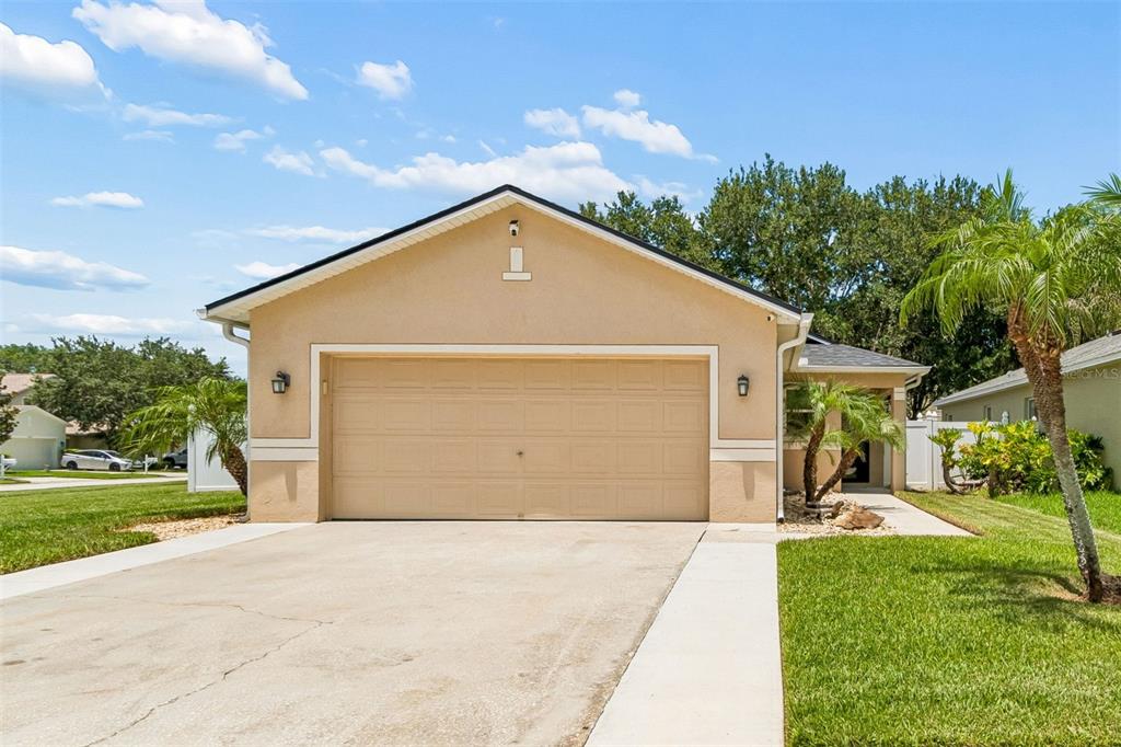 A tan single-story house features a two-car garage, a concrete driveway, and palm trees — 32323 FISH HOOK LOOP, WESLEY CHAPEL, FL