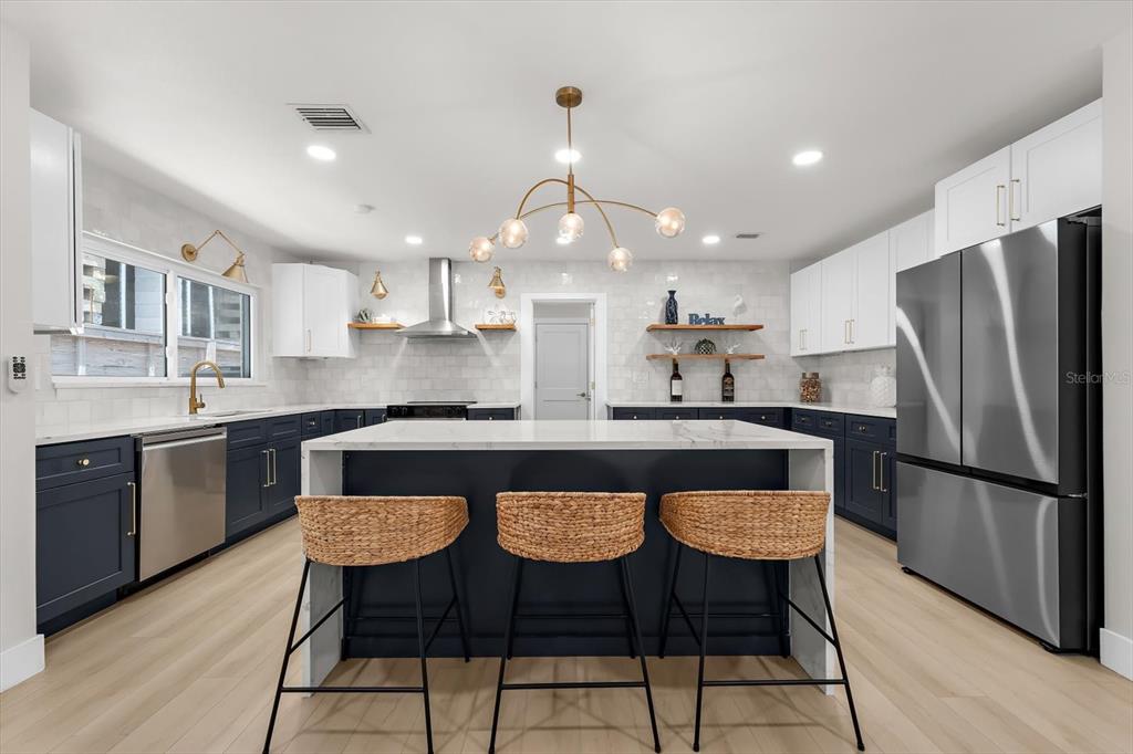 A modern kitchen features a central island with bar stools, navy cabinets, and white countertops — 730 BAY ESPLANADE, CLEARWATER BEACH, FL