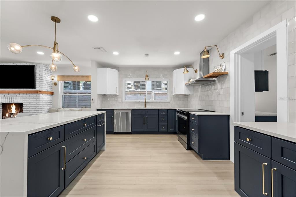 A kitchen features dark blue cabinets, white countertops, a large island, and a brick fireplace — 730 BAY ESPLANADE, CLEARWATER BEACH, FL