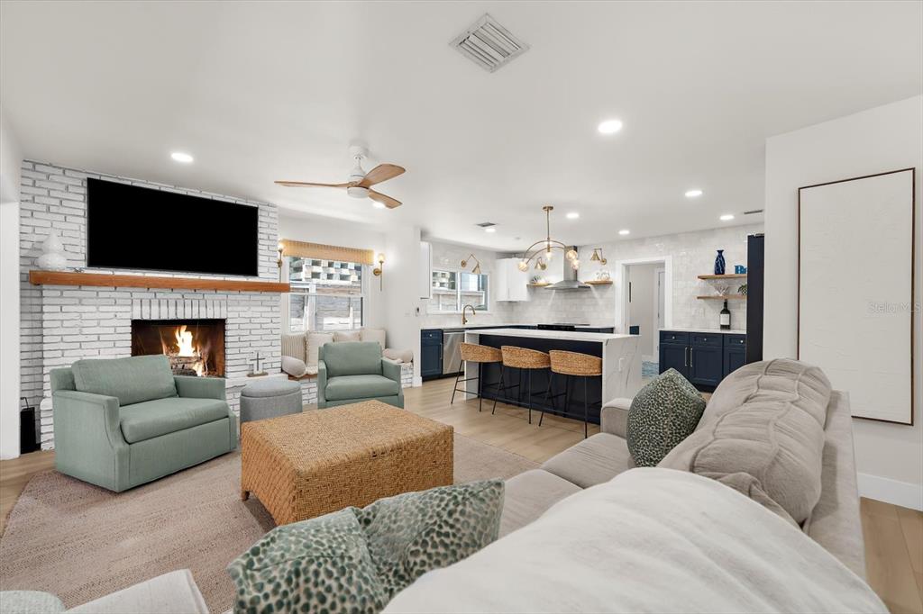 An open-concept living room and kitchen feature a white brick fireplace and a kitchen island — 730 BAY ESPLANADE, CLEARWATER BEACH, FL