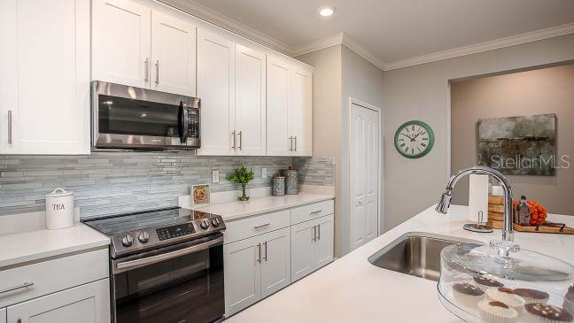 A kitchen features white cabinets, stainless steel appliances, a tiled backsplash, and a center island — 24278 NW 11TH LANE, NEWBERRY, FL