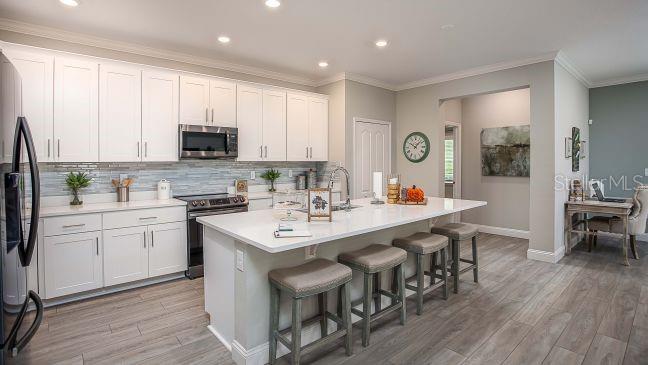 A kitchen with white cabinets, a large island with bar stools, and light wood flooring — 24278 NW 11TH LANE, NEWBERRY, FL