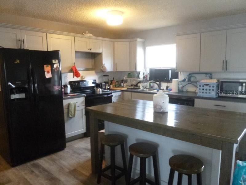 A kitchen features light-colored cabinets, a black refrigerator, and a wooden island with stools — 528 CENTRAL AVENUE, FROSTPROOF, FL