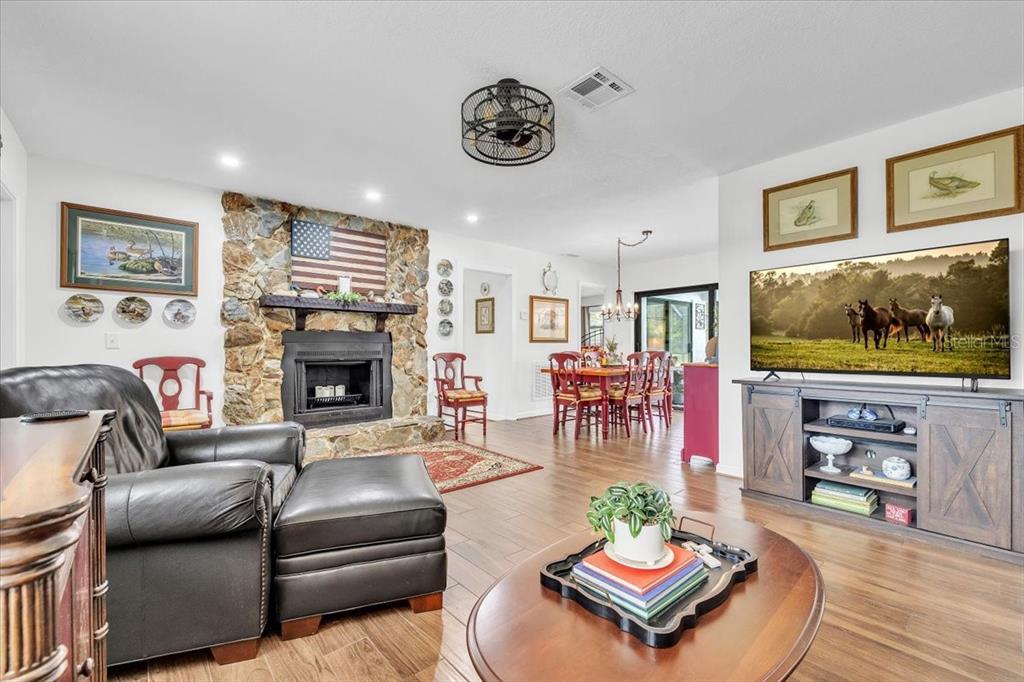 A living room with a stone fireplace, wood-look tile flooring, and a flat-screen television — 4806 SW COUNTY ROAD 769, ARCADIA, FL