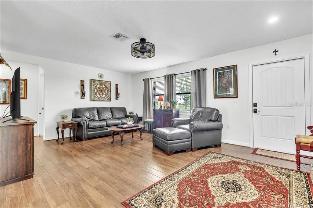 A living room with wood-look flooring, gray leather furniture, and a large patterned area rug — 4806 SW COUNTY ROAD 769, ARCADIA, FL