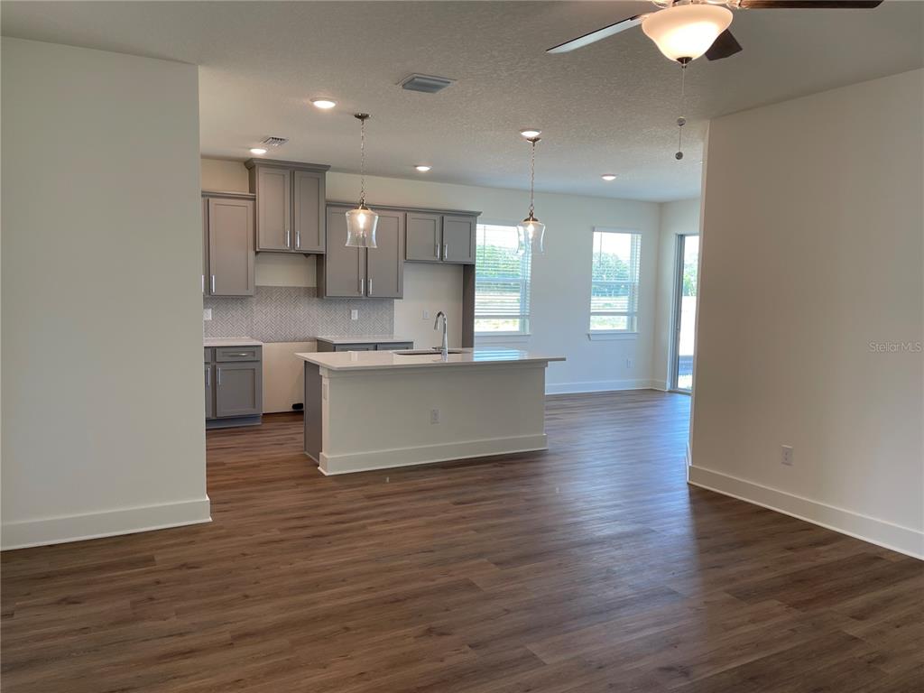 A kitchen with grey cabinets, a white island, and wood-look flooring opens to a living area — 3809 DAYBREAK RUN LOOP, SPRING HILL, FL
