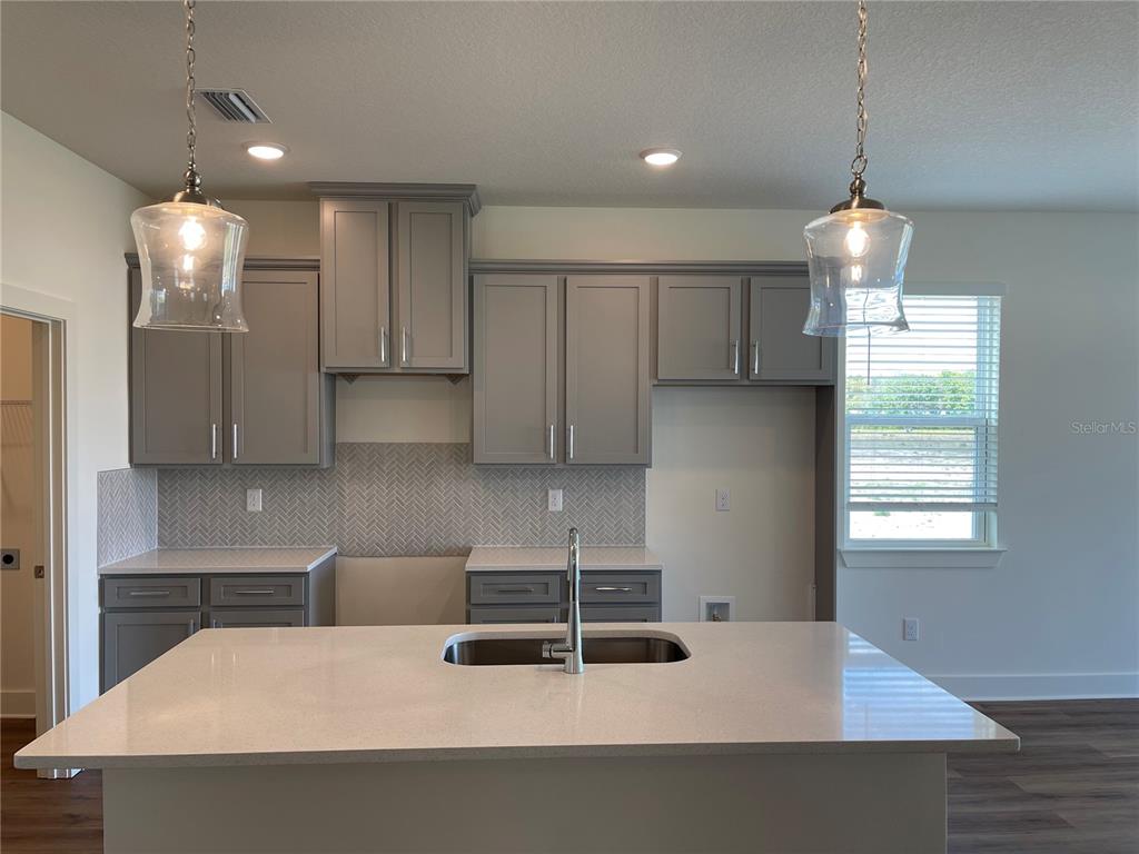 A modern kitchen features gray cabinets, a quartz island with a sink, and pendant lighting — 3809 DAYBREAK RUN LOOP, SPRING HILL, FL