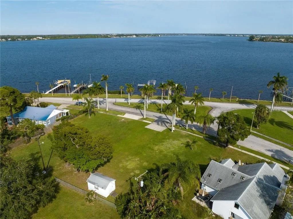 An aerial view shows a grassy lot near a waterfront with docks and palm trees — 2520 RIVERSIDE DRIVE E, BRADENTON, FL