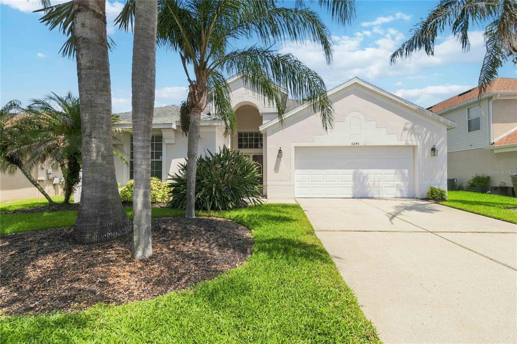A single-story house with a white stucco exterior, a two-car garage, and palm trees — 3245 FALCON POINT DRIVE, KISSIMMEE, FL