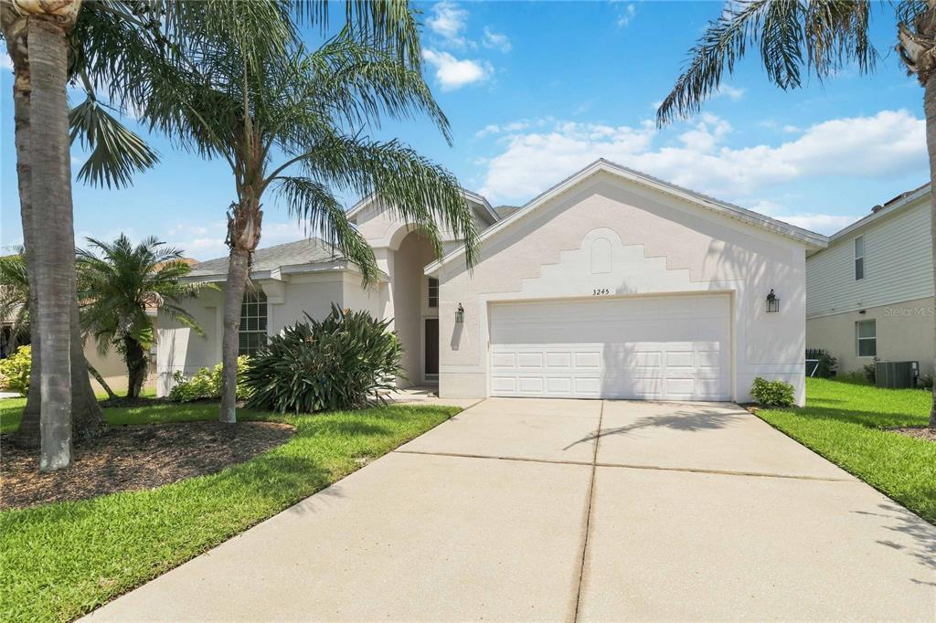 A single-story house with a white stucco exterior, a two-car garage, and palm trees — 3245 FALCON POINT DRIVE, KISSIMMEE, FL