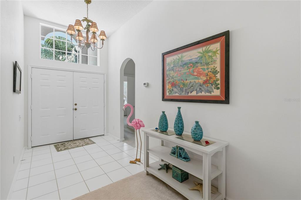 A bright entryway features white tile floors, a white console table, and a flamingo statue — 3245 FALCON POINT DRIVE, KISSIMMEE, FL