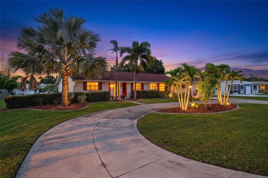 A single-story house with a curved driveway and palm trees at dusk — 22112 BRONXVILLE AVENUE, PORT CHARLOTTE, FL