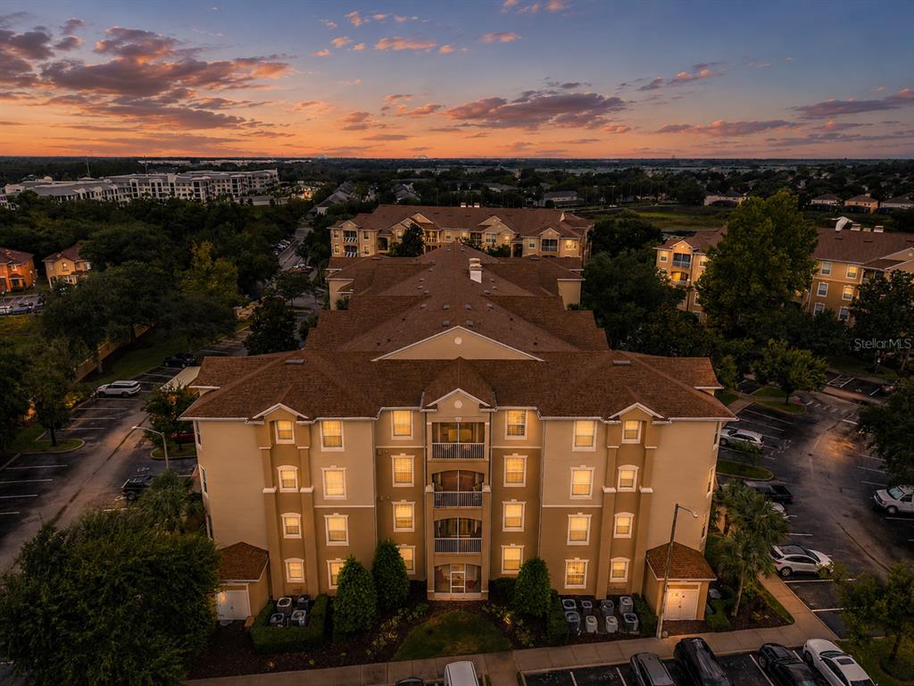 An aerial view of a multi-story apartment building at sunset with surrounding parking lots — 2817 ALMATON LOOP UNIT 402, KISSIMMEE, FL