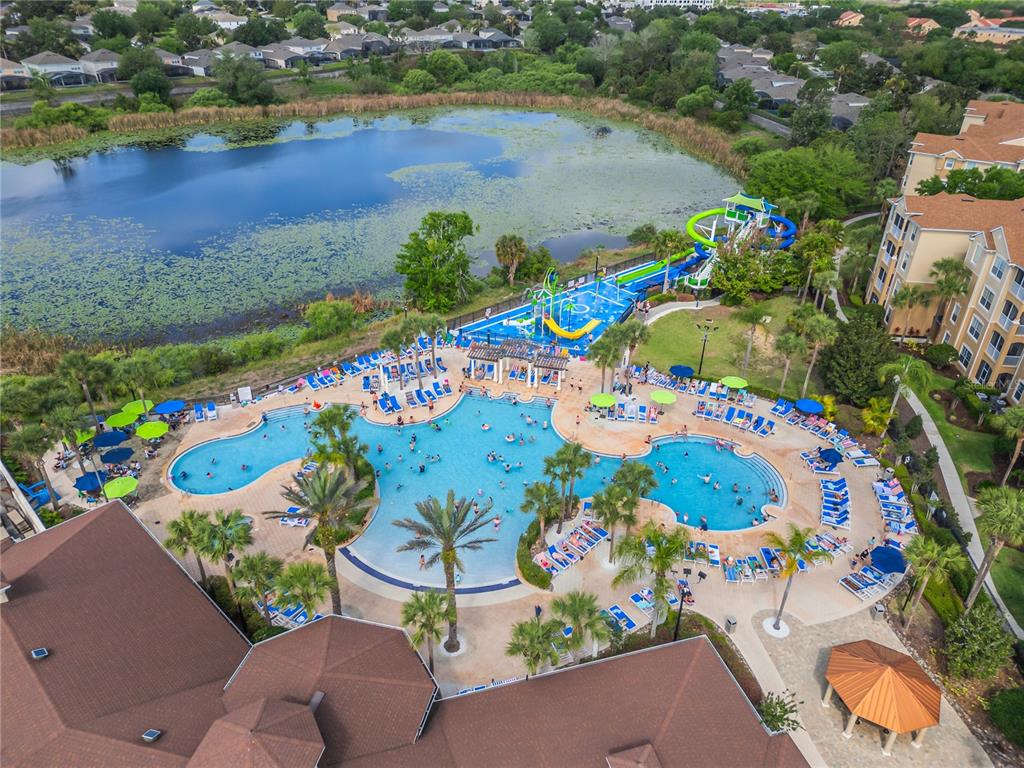 An aerial view shows a large swimming pool complex with water slides next to a lake — 2817 ALMATON LOOP UNIT 402, KISSIMMEE, FL