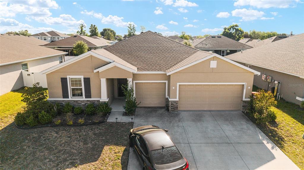 A tan single-story house with a three-car garage and a driveway sits on a lawn — 8285 SW 58TH AVENUE, OCALA, FL