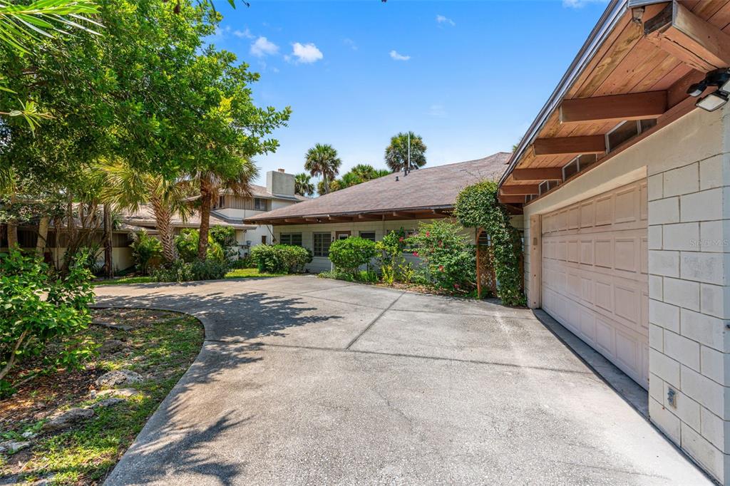 A concrete driveway leads to a one-story house with a garage and surrounding tropical landscaping — 1230 S ORLANDO AVENUE, COCOA BEACH, FL